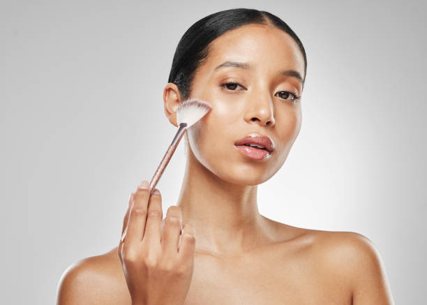 A woman applying bronzer to her cheek with a makeup brush for a glowing look.