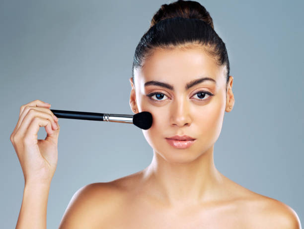 Woman holding a makeup brush to her cheek, demonstrating makeup application.